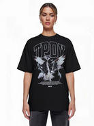 Eine Person steht mit dem Gesicht nach vorne in einem schwarzen trueprodigy Oversize-T-Shirt mit Adlergrafik & TRUEPRODIGY-Schriftzug aus schwerem Jerseystoff. Das Shirt hat eine auffällige Vogelgrafik, ein markantes Branding, einen kleinen weißen Text und einen Barcode am Saum.