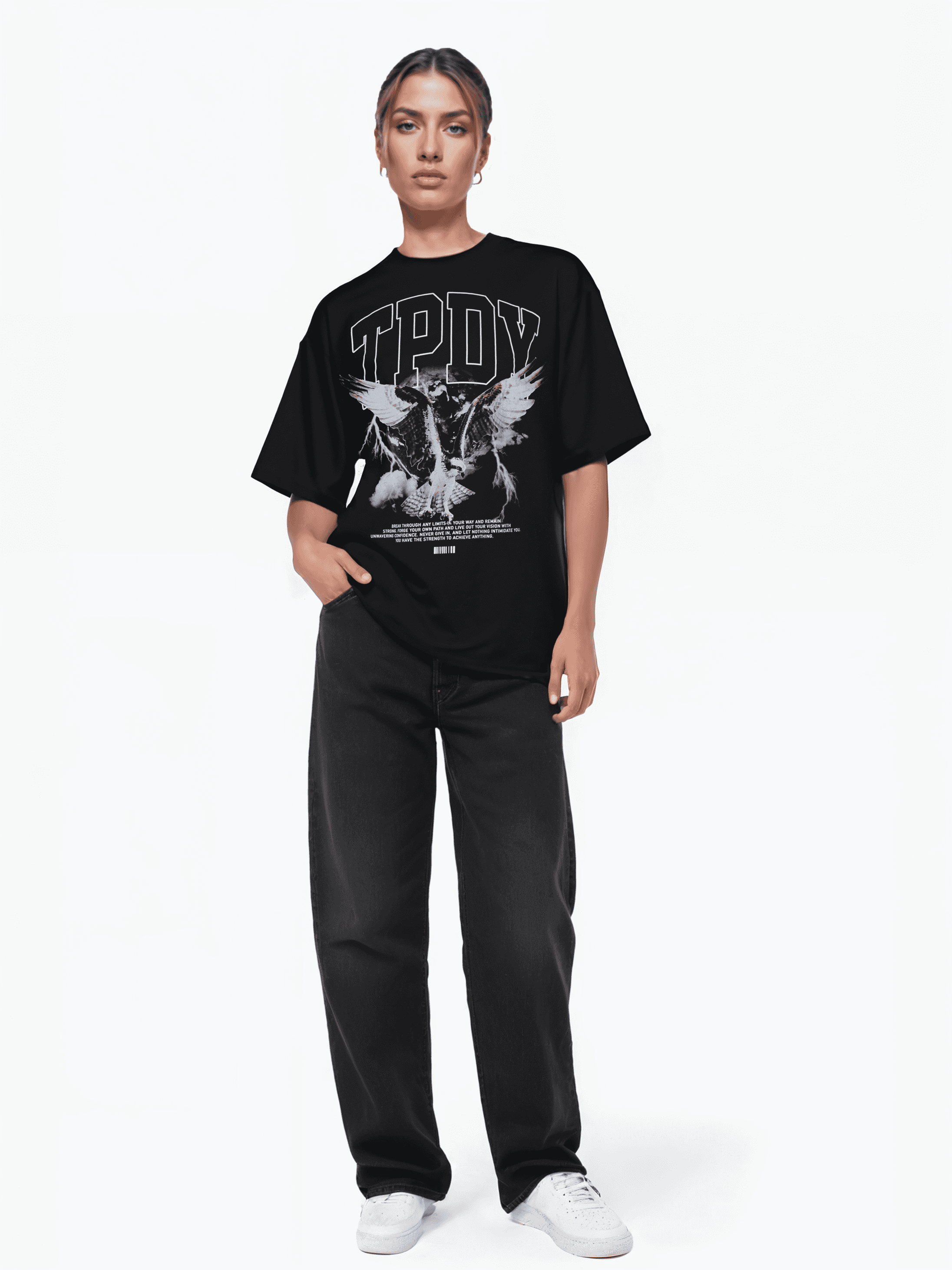 Vor einem schlichten weißen Hintergrund trägt eine Person das Trueprodigy Yuki F Unisex-T-Shirt mit großer Grafik und schwarzen Hosen. Sie verkörpert einen Oversize-Stil mit weißen Turnschuhen und einer Hand in der Tasche. Ihr Gesichtsausdruck ist neutral.