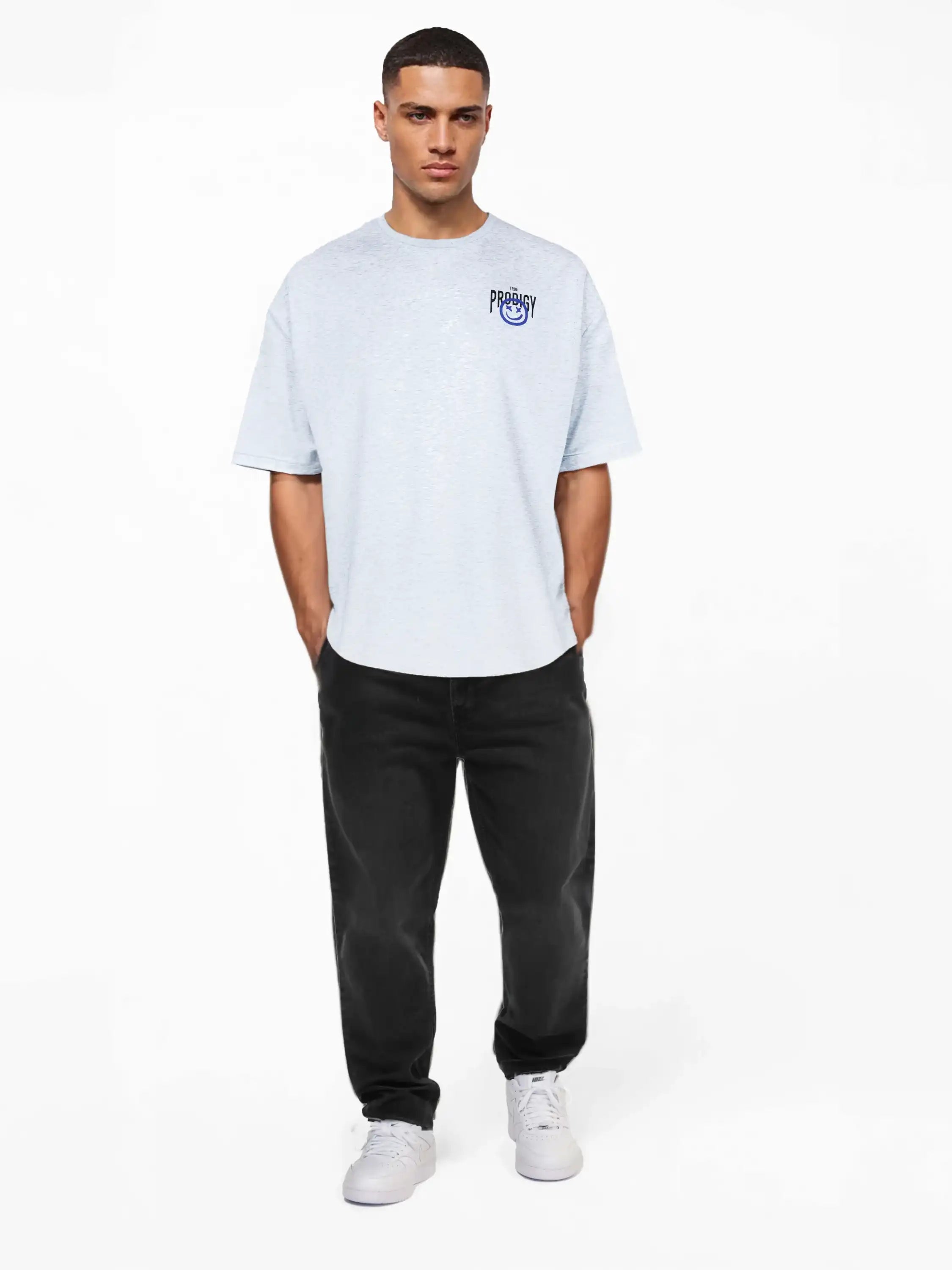 Ein Mann steht vor einem schlichten weißen Hintergrund und trägt das trueprodigy Oversize-T-Shirt mit Spray-Smiley & Rückenprint "Happy Mind" mit kleiner blauer Brustgrafik, gepaart mit schwarzer Jeans und weißen Turnschuhen, die Hände in den Taschen, den Blick nach vorne gerichtet.
