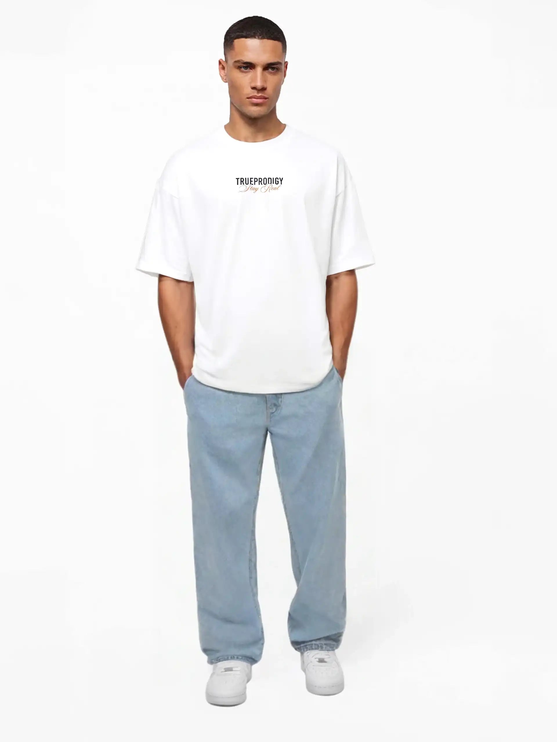 Ein Mann steht mit dem Gesicht nach vorne, trägt ein lockeres weißes Lou Oversize-T-Shirt mit Schriftzug & "Stay Real" Front- & Rückenprint von trueprodigy, hellblaue Baggy Jeans und weiße Turnschuhe. Seine Hände stecken in den Taschen vor einem schlichten weißen Hintergrund.