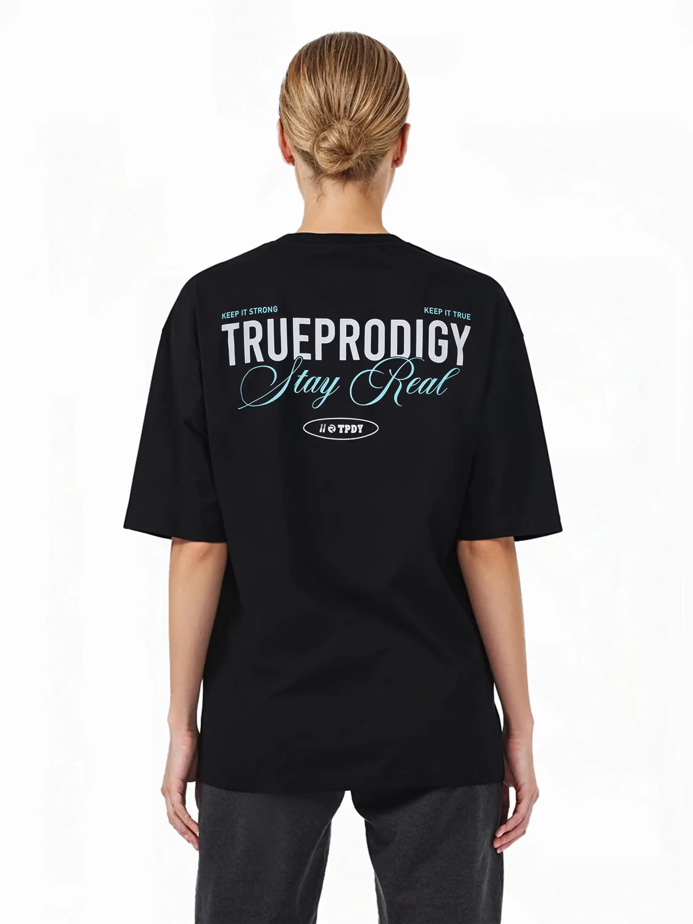 Eine Person mit blonden Haaren in einem tiefen Dutt ist von hinten zu sehen. Sie trägt das trueprodigy Oversize-T-Shirt mit "Stay Real" Schriftzug vorne & hinten, mit weißem und hellblauem Text auf schwerem Jerseystoff.