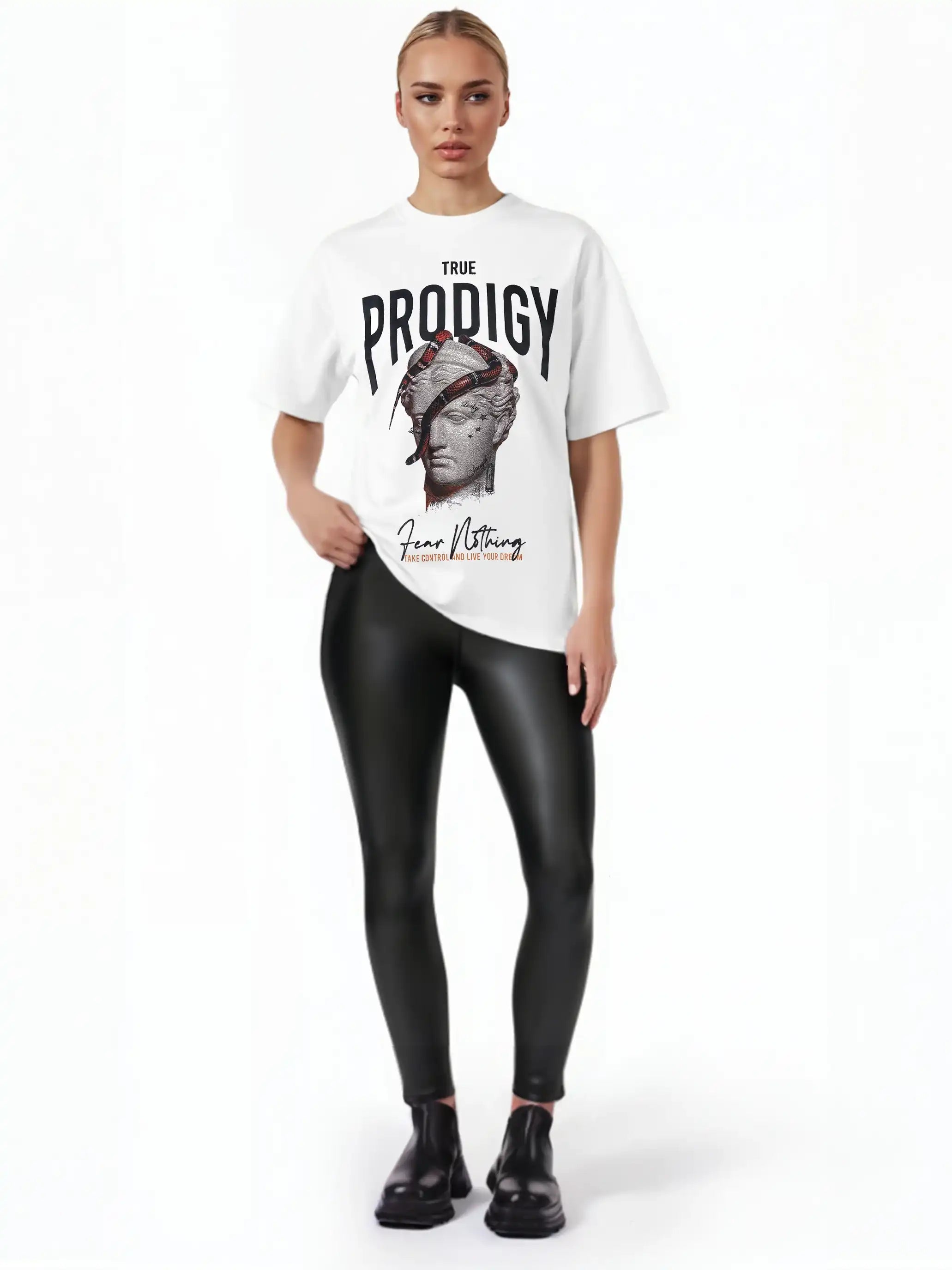 Eine Frau posiert vor einem weißen Hintergrund in dem trueprodigy Jamie F Oversize-T-Shirt mit Skulptur-Grafik, Schlangen- und "Fear Nothing"-Print, gepaart mit schwarzen Leggings in Lederoptik und schwarzen Ankle Boots.
