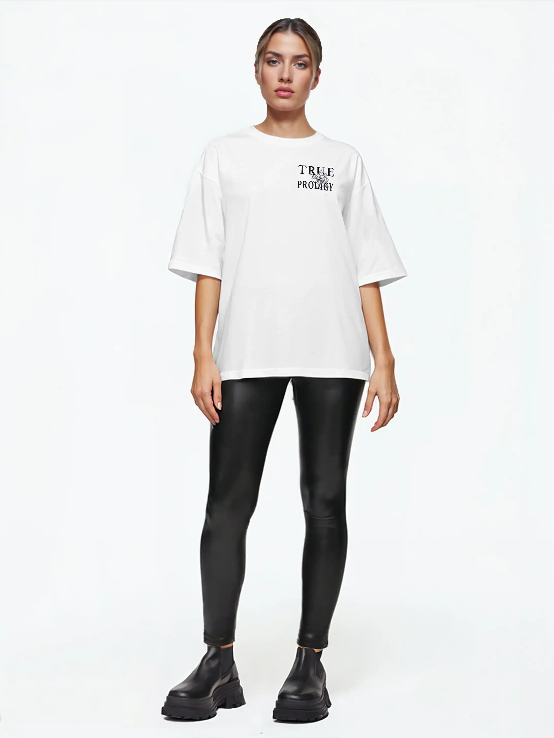 Eine Person steht mit Blick nach vorne in einem weißen trueprodigy Alex F Oversize-T-Shirt mit Spray-Smiley & trueprodigy-Schriftzug auf Vorder- und Rückseite, schwarzen Kunstleder-Leggings und klobigen schwarzen Stiefeln vor einem schlichten weißen Hintergrund.