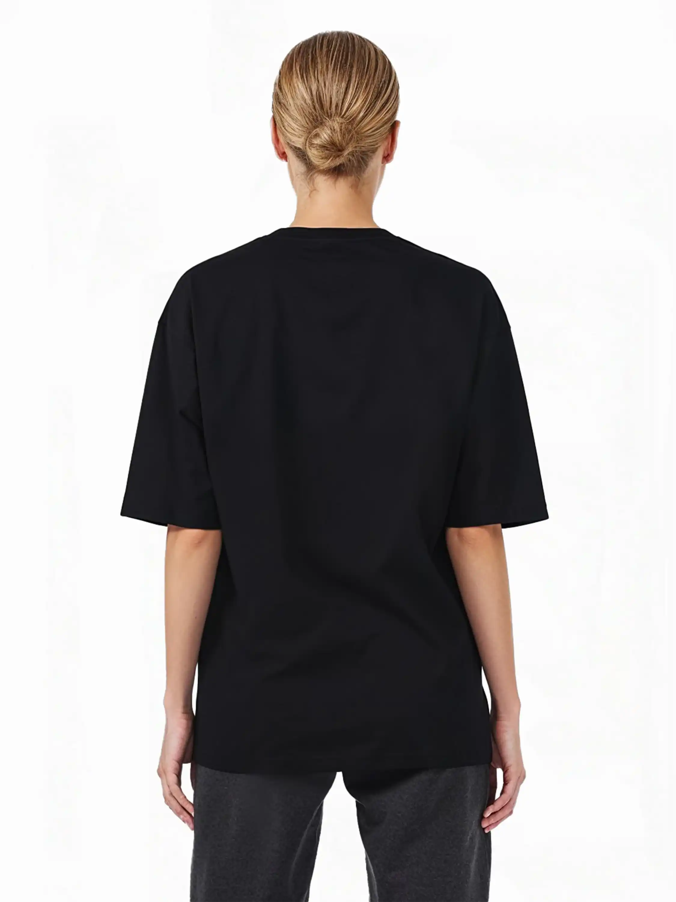 Eine Person mit hellen Haaren in einem tiefen Dutt ist von hinten zu sehen. Sie trägt das trueprodigy Haram F Oversize-T-Shirt mit TPDY-Stickerei & cleaner Optik und eine dunkle Hose vor einem schlichten weißen Hintergrund.