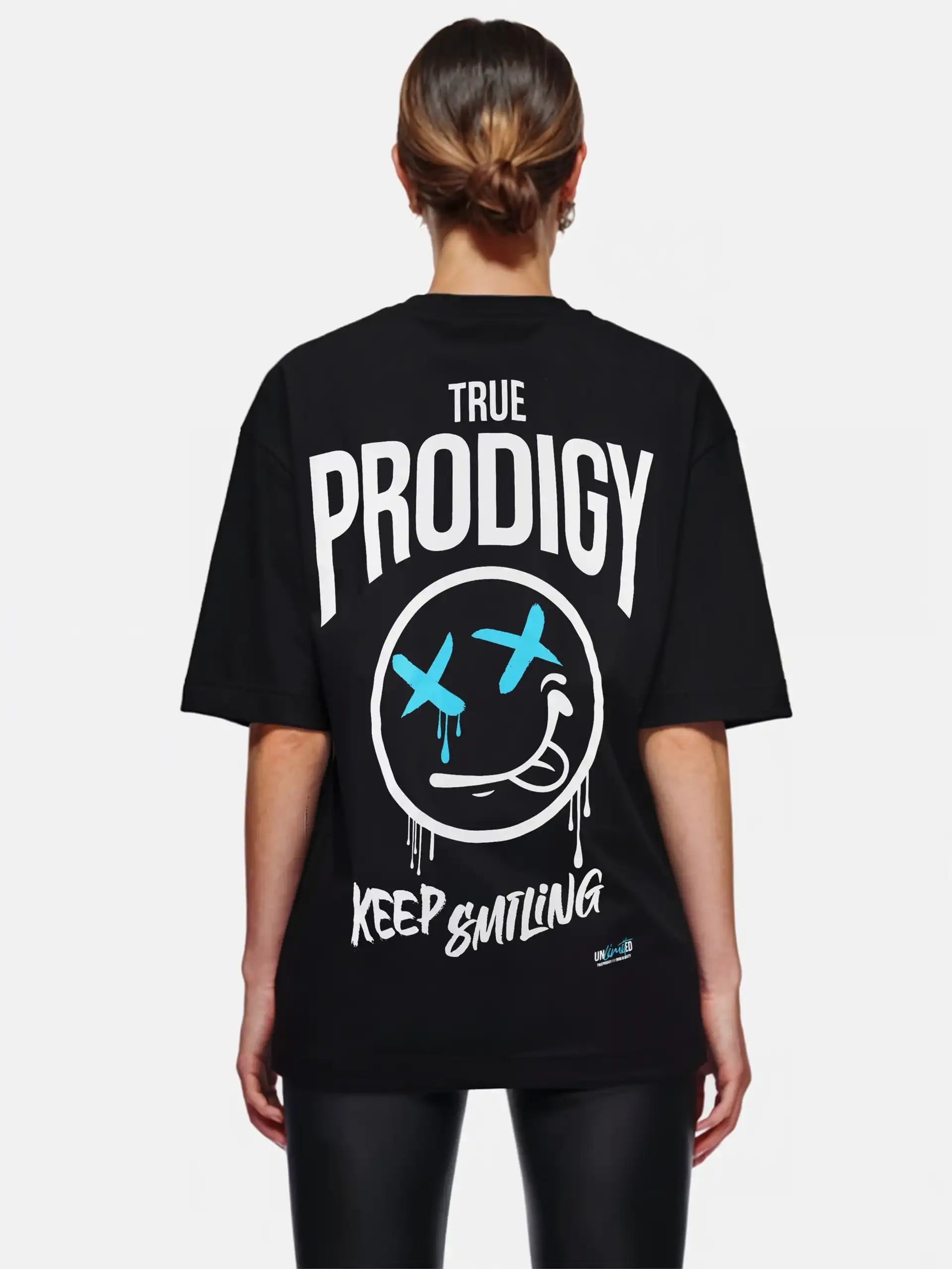 Eine Person mit hellbraunem, nach hinten gebundenem Haar trägt ein schwarzes Trueprodigy Kenji F Oversize-Damen-T-Shirt mit Graffiti-Aufdrucken und einer großen Distressed Face-Grafik mit blauen X-Augen und einem Stirnrunzeln auf dem Rücken.