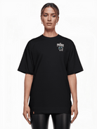 Eine Person steht vor weißem Hintergrund und trägt das Kenji Oversized T-Shirt mit Druck von trueprodigy. Es besteht aus schwerem Jerseystoff und trägt oben links ein kleines Logo und den Schriftzug „PRODIGY“. Mit zurückgebundenen Haaren und einer schwarzen Hose ist es mühelos unisex.