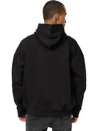 Gezeigt wird eine Person von hinten, die entspannt in einem schwarzen trueprodigy Tobi Oversized Hoodie mit Print und dunkler Jeans steht. Die Kapuze des Unisex Kapuzensweatshirts ist hochgezogen, bedeckt aber nicht ihren Kopf.