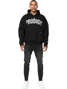 Ein Mann steht mit dem Gesicht nach vorne und trägt einen trueprodigy Tobi Oversized Hoodie mit Print, schwarze Jeans und weiße Turnschuhe vor einem schlichten weißen Hintergrund.