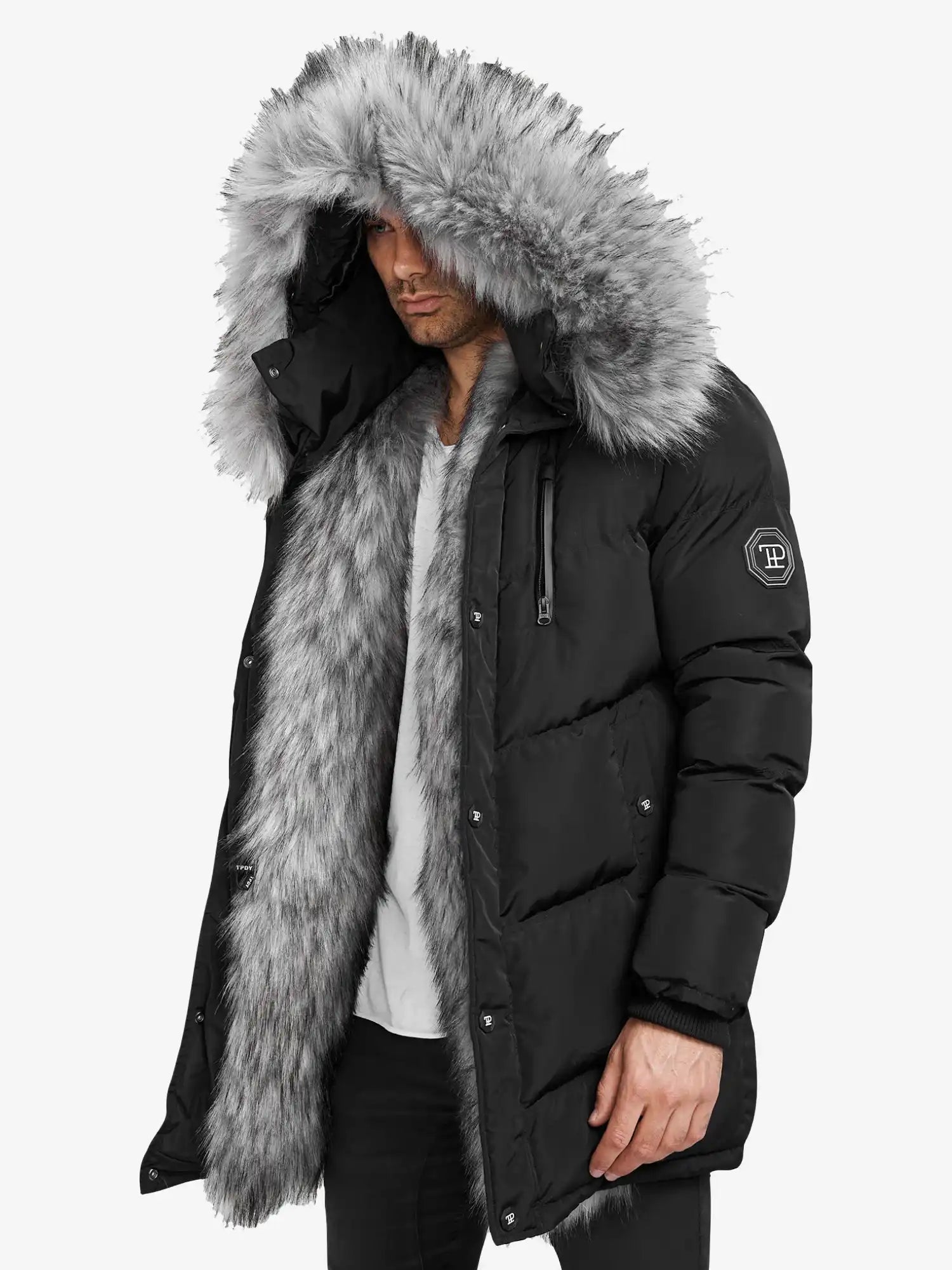 Ein Mann trägt die Zayn Winterjacke mit Kunstfell von trueprodigy, einen schwarzen, wasserabweisenden Herrenparka mit einem großen grauen Kunstfell-Kapuzenbesatz, Logo-Patch am Ärmel, vor einem schlichten weißen Hintergrund.