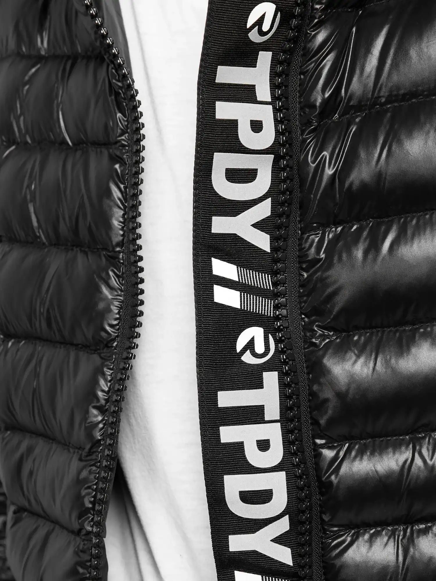 Nahaufnahme der schwarzen, glänzenden Adan Steppjacke mit Kapuze von trueprodigy. Der teilweise geöffnete wasserabweisende Reißverschluss gibt den Blick auf den weißen Stoff darunter frei, und das schwarze Reißverschlussfutter ist mit weißem TPDY-Text und -Logos versehen.