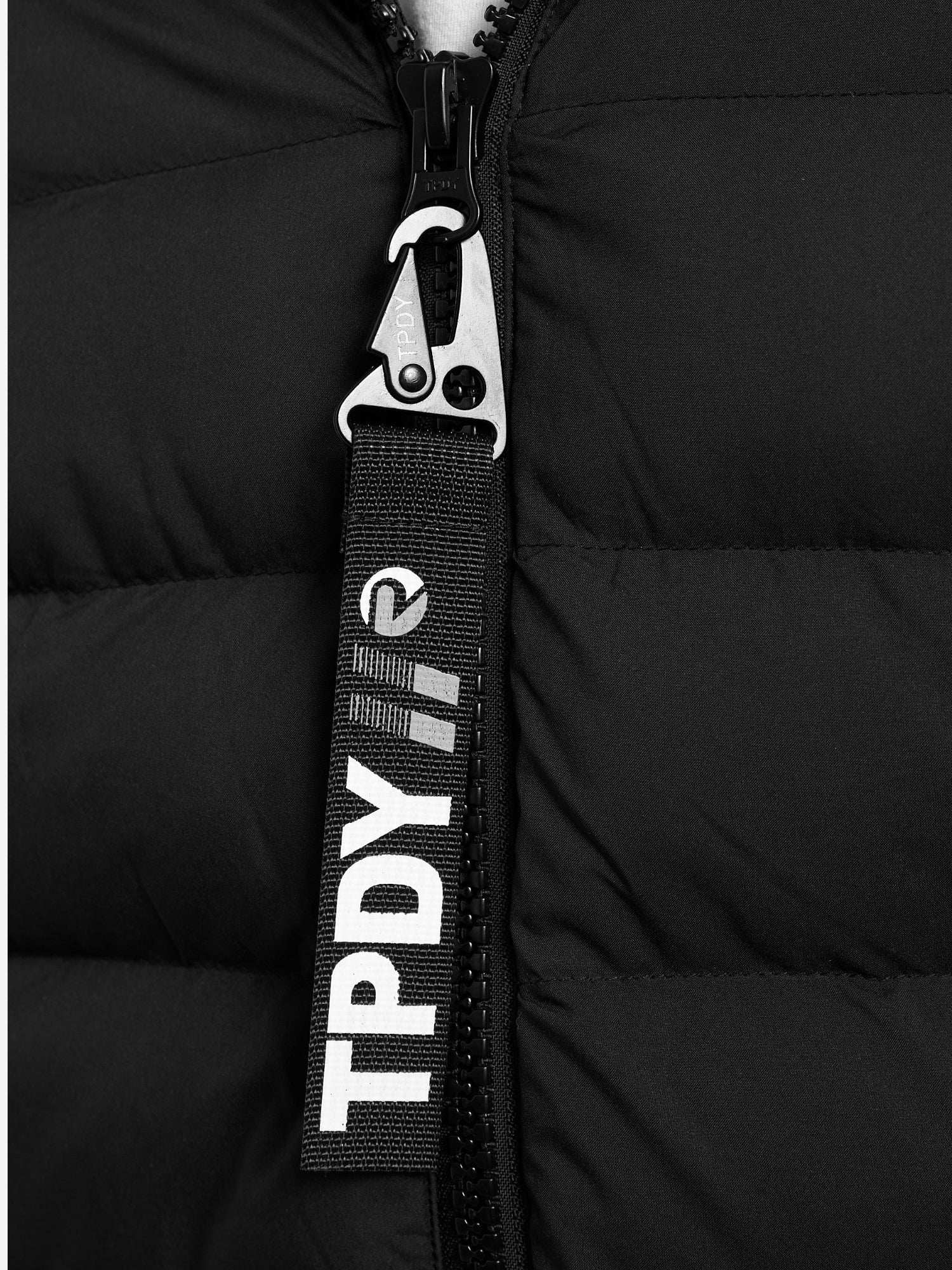 Nahaufnahme der Neo Kurze Pufferjacke mit Logo von trueprodigy: eine schwarze Steppjacke mit Metallreißverschluss und einer schwarzen Stofflasche mit "TPDY" und Logo in Weiß. Diese wasserabweisende Jacke ist ideal für unvorhersehbares Wetter.