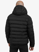 Eine Person trägt die Neo Kurze Pufferjacke mit Logo von trueprodigy in Schwarz, wasserabweisend und mit Kapuze. Die horizontale Steppung ist sichtbar, die Person steht entspannt mit den Armen an den Seiten, von hinten gesehen.