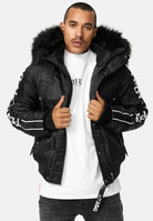 Ein Mann, der die trueprodigy Jonathan Bomberjacke mit Kapuze und Kunstfell, ein weißes T-Shirt und eine dunkle Jeans trägt, steht vor der Kamera und hält seine Jacke offen.