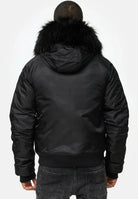 Eine Person steht mit dem Rücken zur Kamera und trägt die trueprodigy Jonathan Bomberjacke mit Kapuze und Kunstfell und dunkle Jeans. Der Hintergrund ist einfarbig und hell.