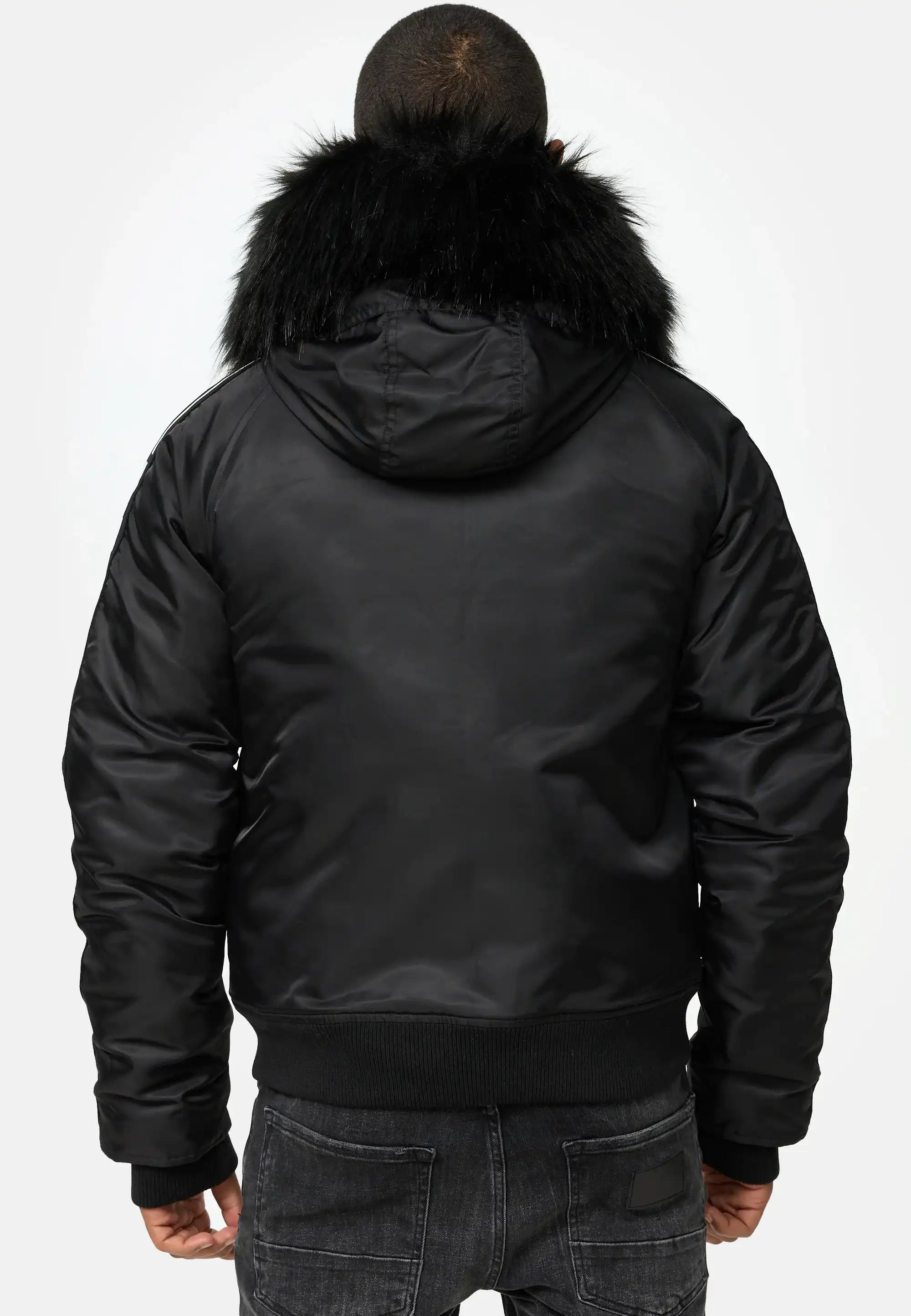Eine Person steht mit dem Rücken zur Kamera und trägt die trueprodigy Jonathan Bomberjacke mit Kapuze und Kunstfell und dunkle Jeans. Der Hintergrund ist einfarbig und hell.