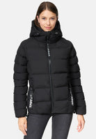Eine Person trägt die Murphy F Matte Steppjacke mit Kapuze von trueprodigy in Schwarz mit Frontreißverschluss und zwei Taschen. Die wasserabweisende Jacke zeigt einen TPDY-Aufdruck vor hellem, schlichten Hintergrund.