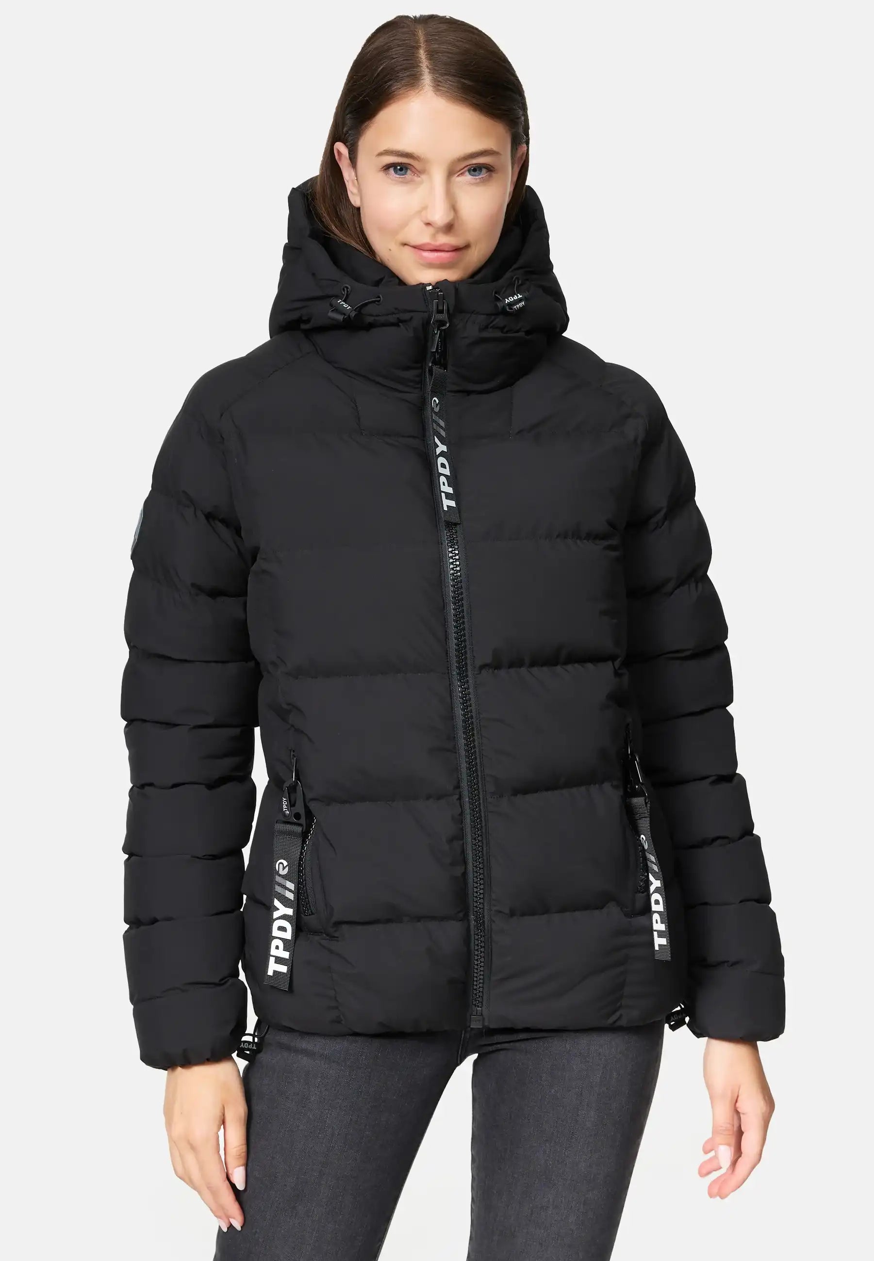 Eine Person trägt die Murphy F Matte Steppjacke mit Kapuze von trueprodigy in Schwarz mit Frontreißverschluss und zwei Taschen. Die wasserabweisende Jacke zeigt einen TPDY-Aufdruck vor hellem, schlichten Hintergrund.