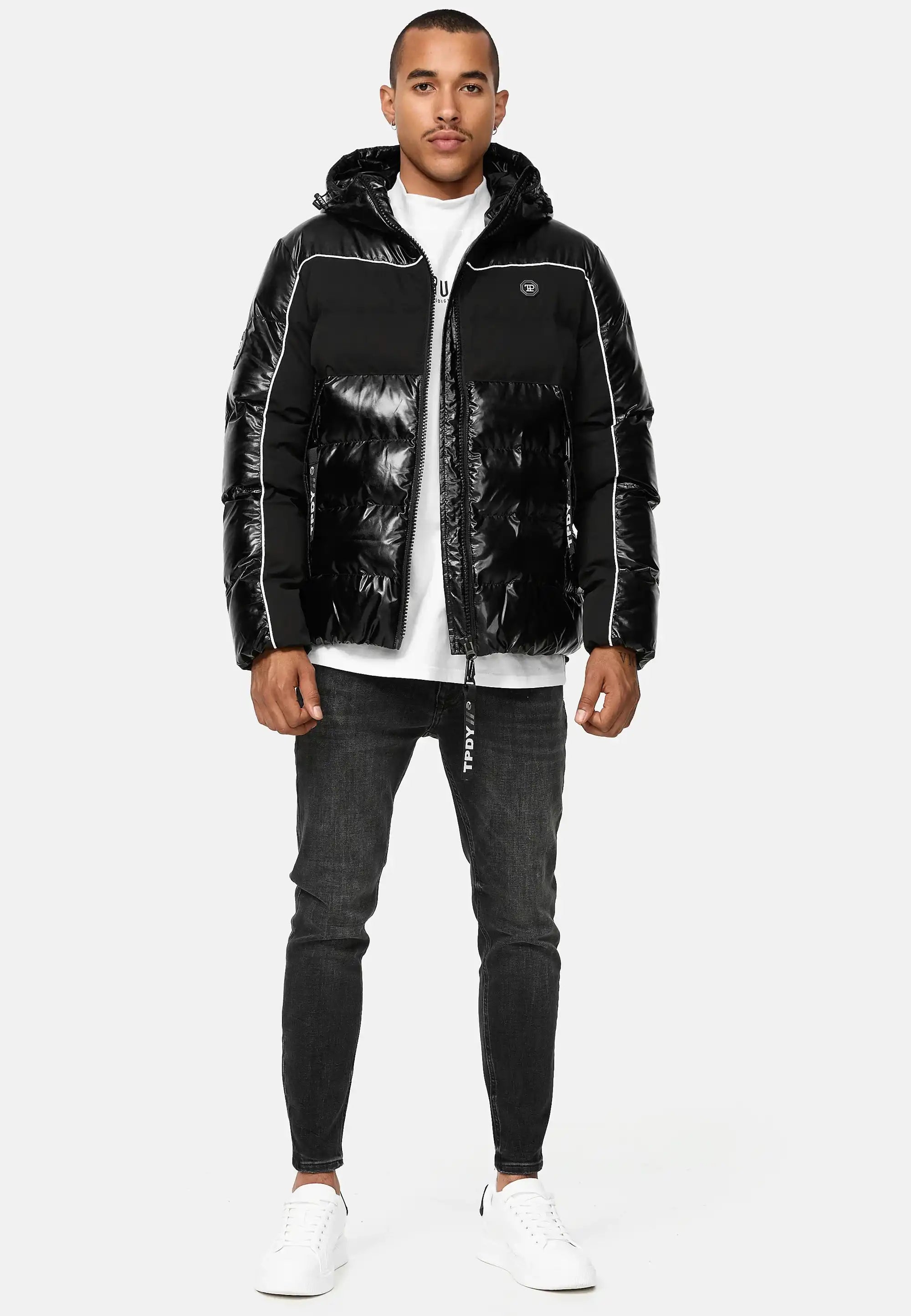Ein Mann steht mit dem Gesicht nach vorne und trägt die trueprodigy Clark Winterjacke mit Kapuze und Logo, ein weißes T-Shirt, dunkle Skinny Jeans und weiße Turnschuhe vor einem schlichten hellen Hintergrund.