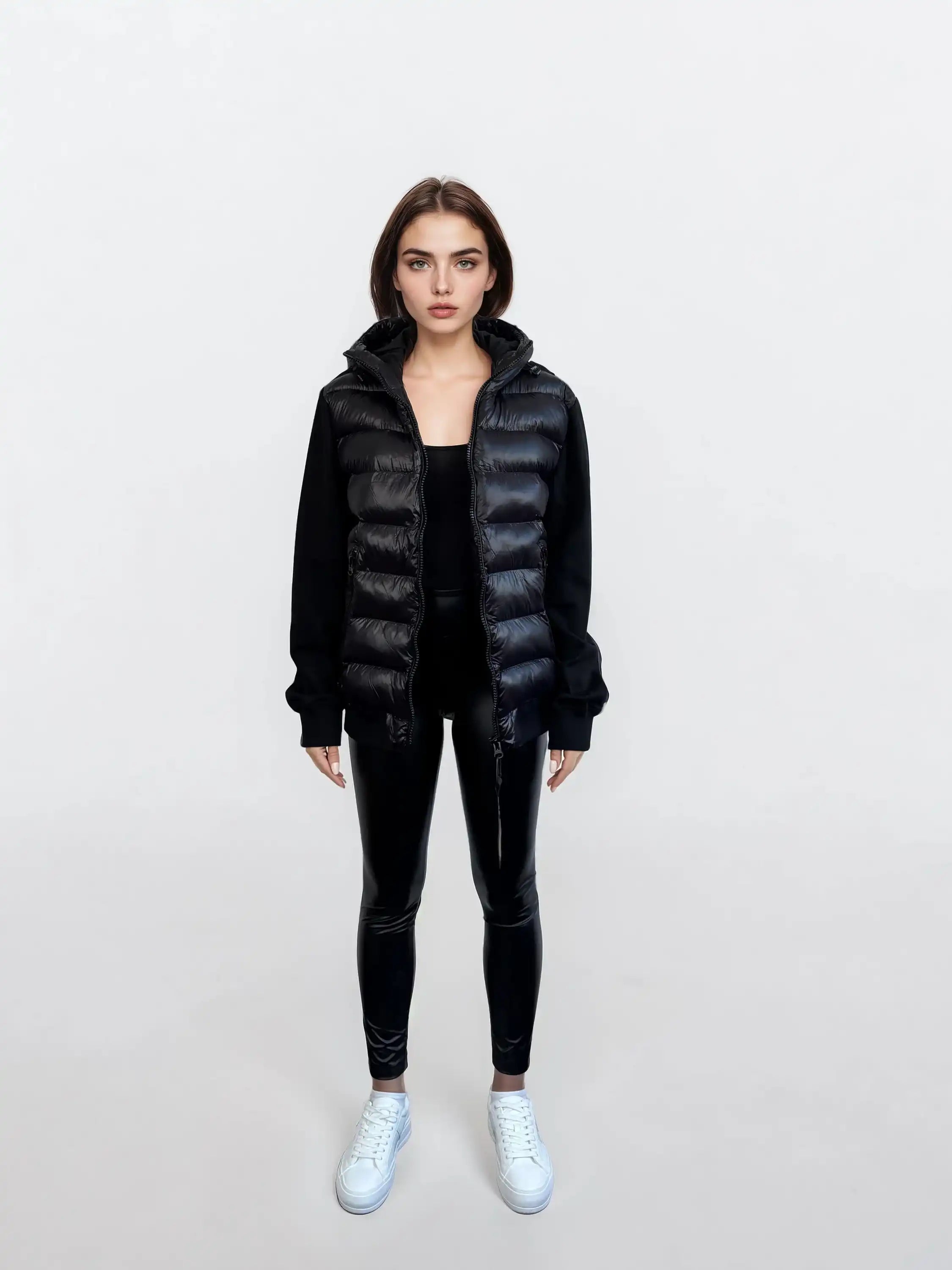 Eine Frau steht vor weißem Hintergrund und trägt eine Oversized Damen Bomber Jacke im urbanen Materialmix-Design von trueprodigy über einem schwarzen Longsleeve, dazu schwarze Leggings und weiße Sneaker. Sie hat glattes braunes Haar und einen neutralen Blick.