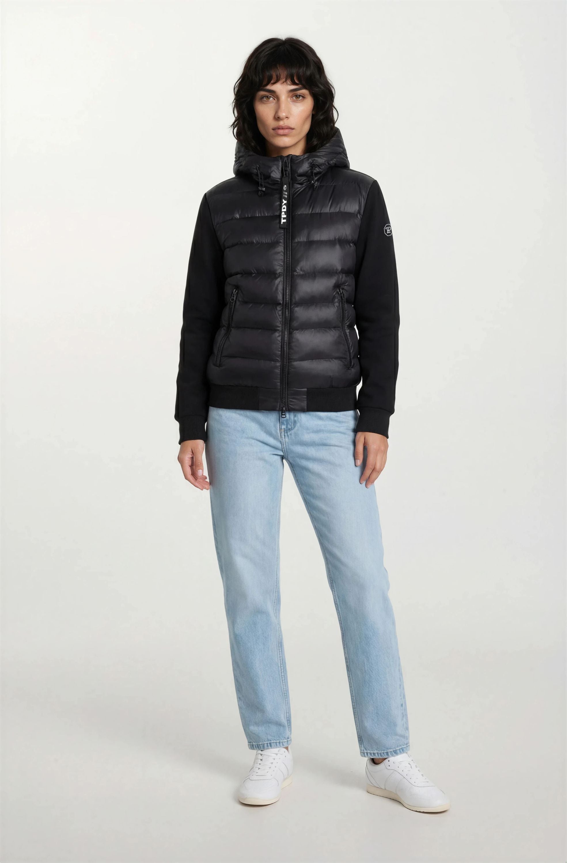 Eine Person, die eine trueprodigy Oversized Damen Bomberjacke im urbanen Materialmix-Design, hellblaue Jeans und weiße Turnschuhe trägt, steht mit dem Gesicht nach vorne vor einem schlichten weißen Hintergrund.