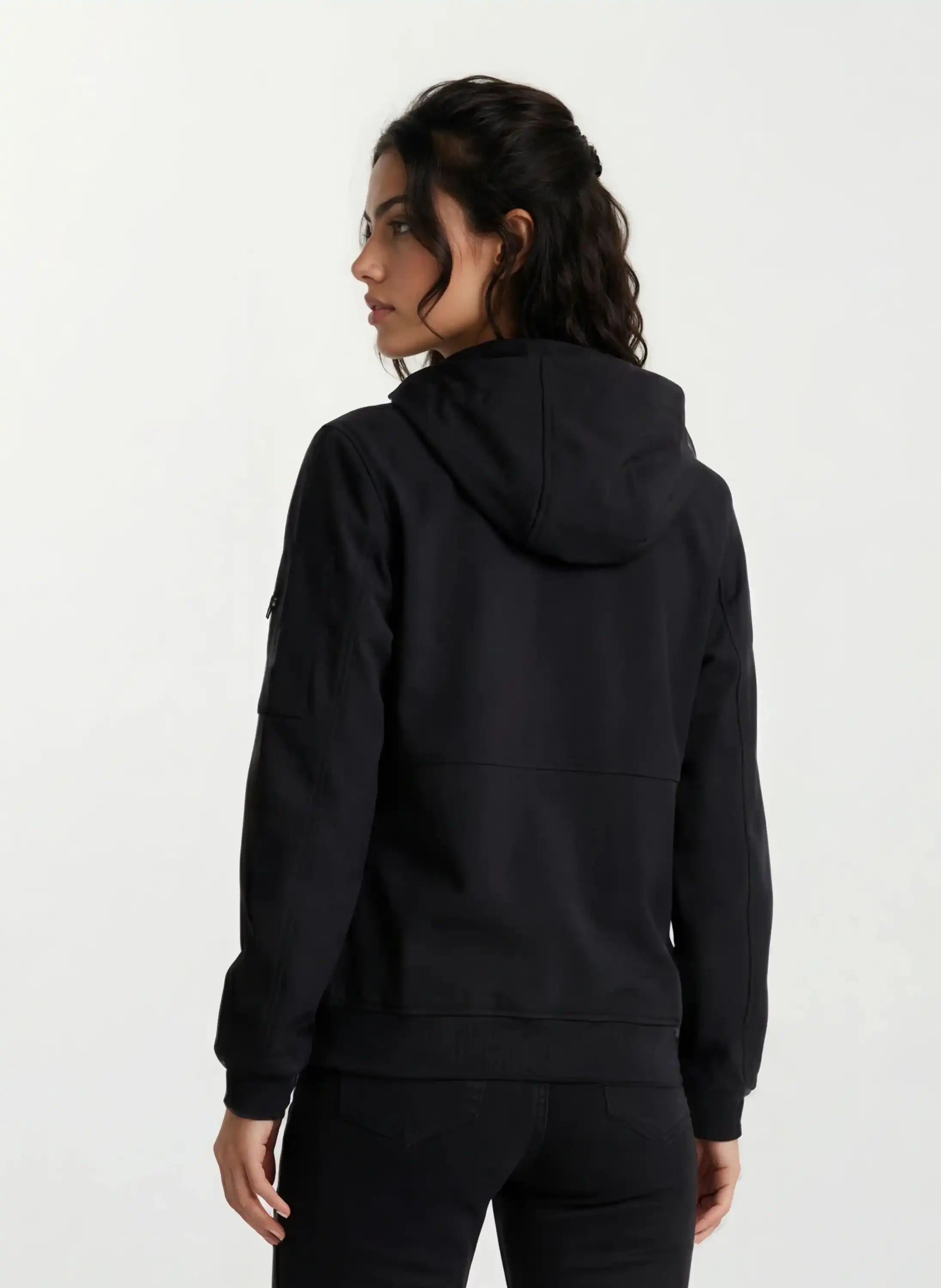 Eine Person mit dunklen Haaren, die eine schwarze Leichte Herrenjacke mit Brust- und Ärmelbadge von trueprodigy und eine schwarze Hose trägt, steht mit dem Gesicht zur Seite vor einem schlichten weißen Hintergrund.