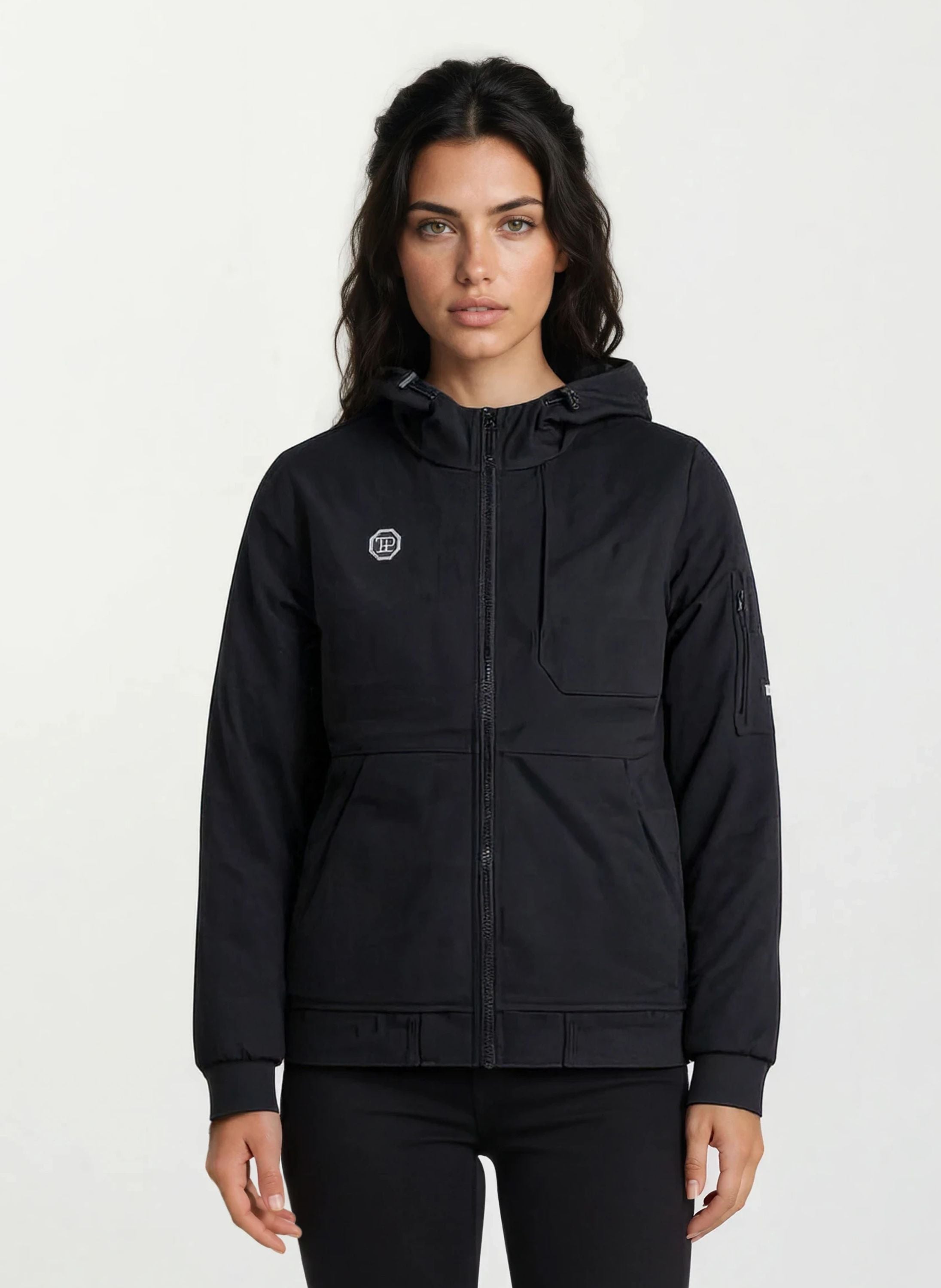 Eine Person mit langen dunklen Haaren trägt eine Trueprodigy Leichte Herrenjacke mit Brust- und Ärmelbadge, die mit einem Frontreißverschluss und mehreren Taschen versehen ist, vor einem schlichten hellen Hintergrund.