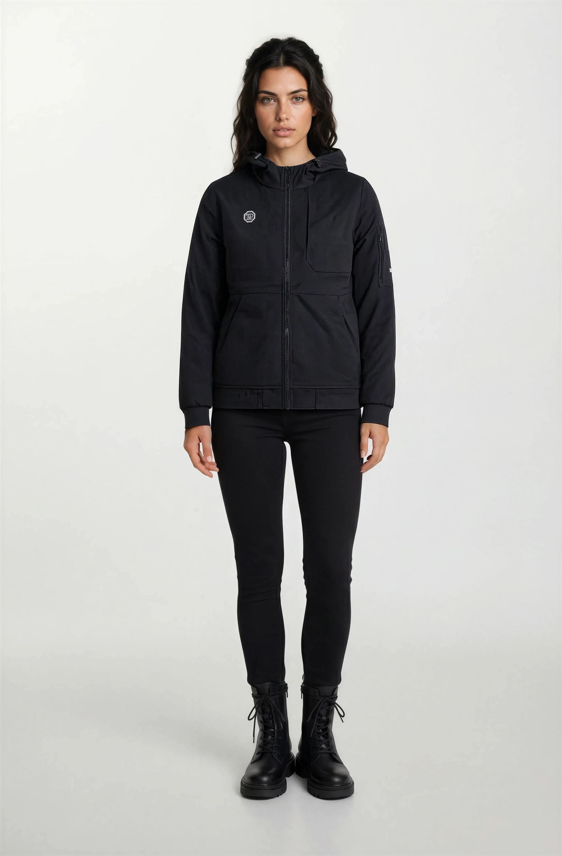 Eine Person steht mit dem Gesicht nach vorne vor einem schlichten Hintergrund. Sie trägt die Trueprodigy Leichte Herrenjacke mit Brust- und Ärmelbadge, passende schwarze Hosen und Schnürstiefel. Die Hände liegen entspannt an der Seite.