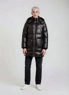 Eine Person mit kurzen blonden Haaren sieht nach vorne und trägt eine glänzende trueprodigy Herren Winterjacke mit abnehmbarer Kapuze im Regular Fit, eine schwarze Hose und weiße Turnschuhe vor einem schlichten hellen Hintergrund.