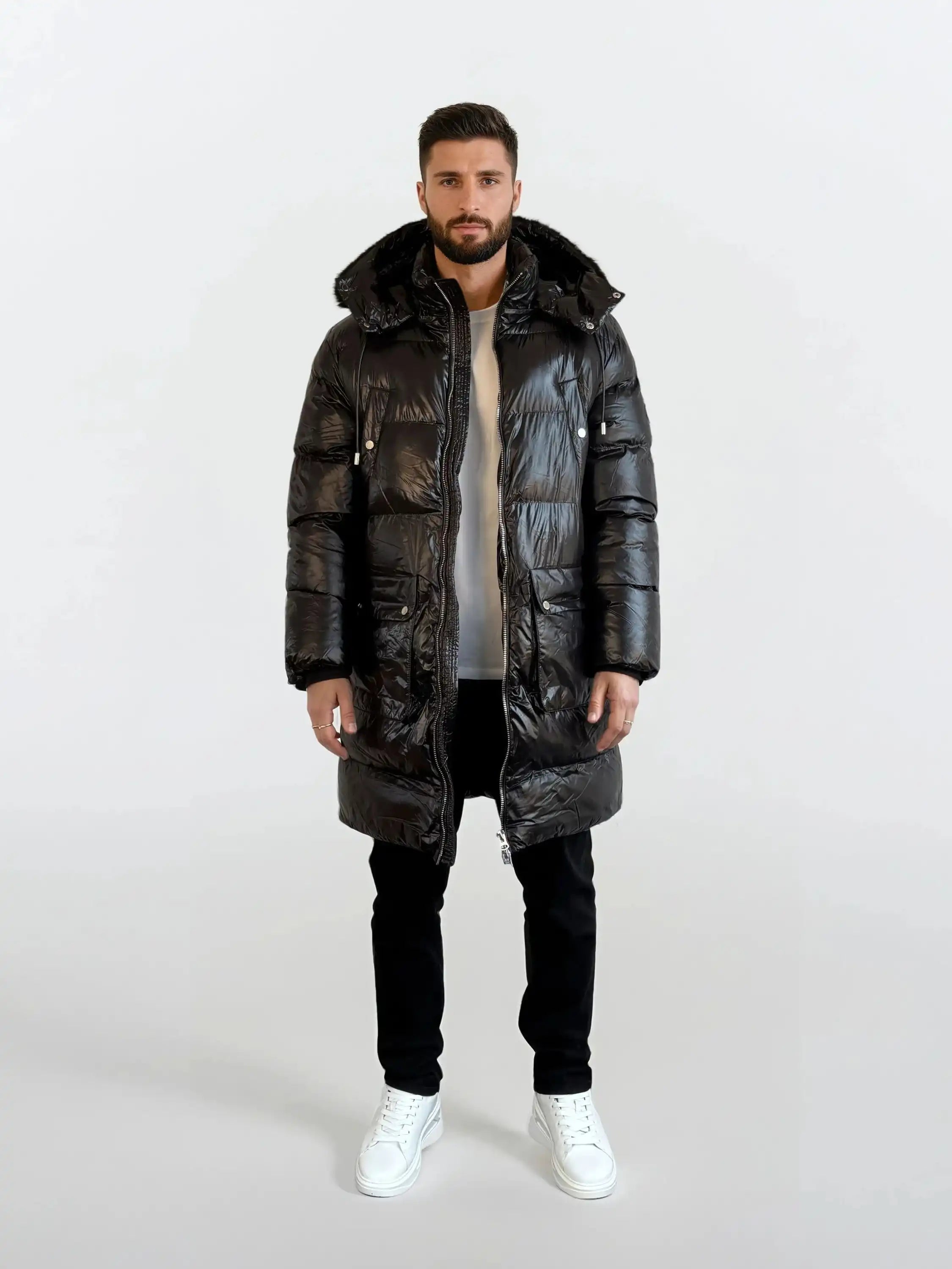 Ein Mann steht mit dem Gesicht nach vorne und trägt eine glänzende trueprodigy Herren Winterjacke mit abnehmbarer Kapuze im Regular Fit über einem weißen Hemd, einer schwarzen Hose und weißen Turnschuhen vor einem schlichten weißen Hintergrund.
