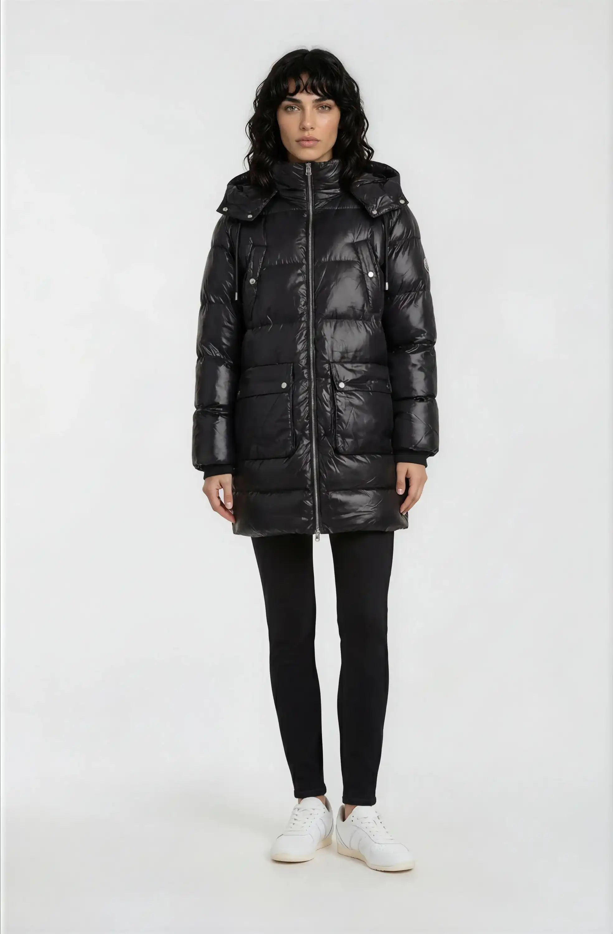 Eine Person mit schulterlangen dunklen Haaren trägt die trueprodigy Damen Winterjacke mit abnehmbarer Kapuze im Regular Fit, gepaart mit schwarzen Leggings und weißen Sneakers, vor einem schlichten weißen Hintergrund.