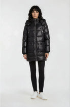 Eine Person mit schulterlangen dunklen Haaren trägt die trueprodigy Damen Winterjacke mit abnehmbarer Kapuze im Regular Fit, gepaart mit schwarzen Leggings und weißen Sneakers, vor einem schlichten weißen Hintergrund.
