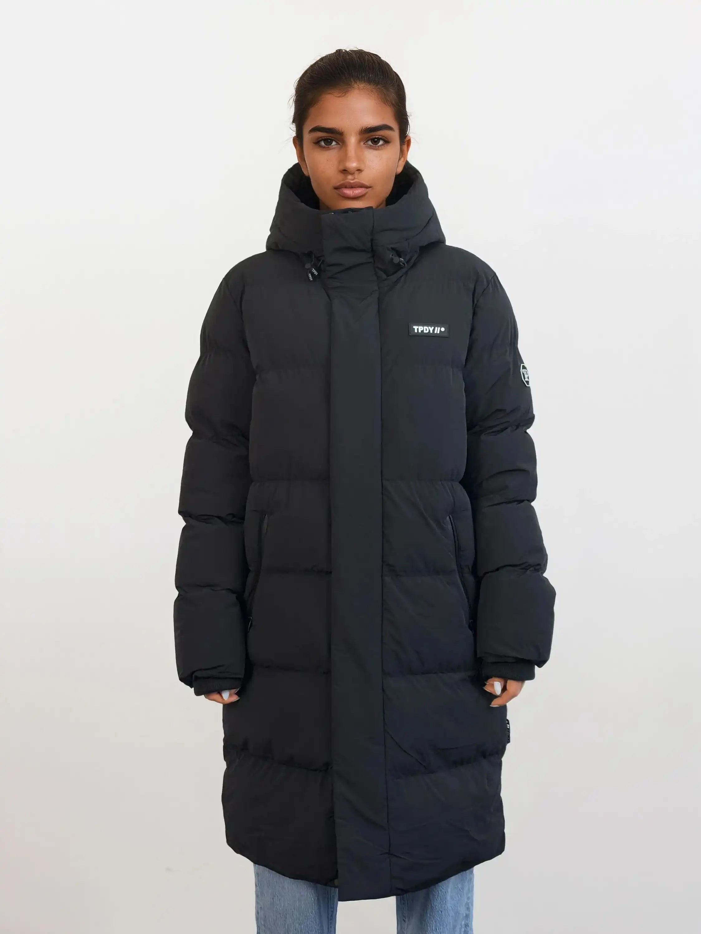 Eine Person steht mit dem Gesicht nach vorne und trägt den trueprodigy Damen Parka mit fester Kapuze im Regular Fit mit sichtbarem Brustlogo, gepaart mit einer hellblauen Jeans vor einem schlichten weißen Hintergrund.