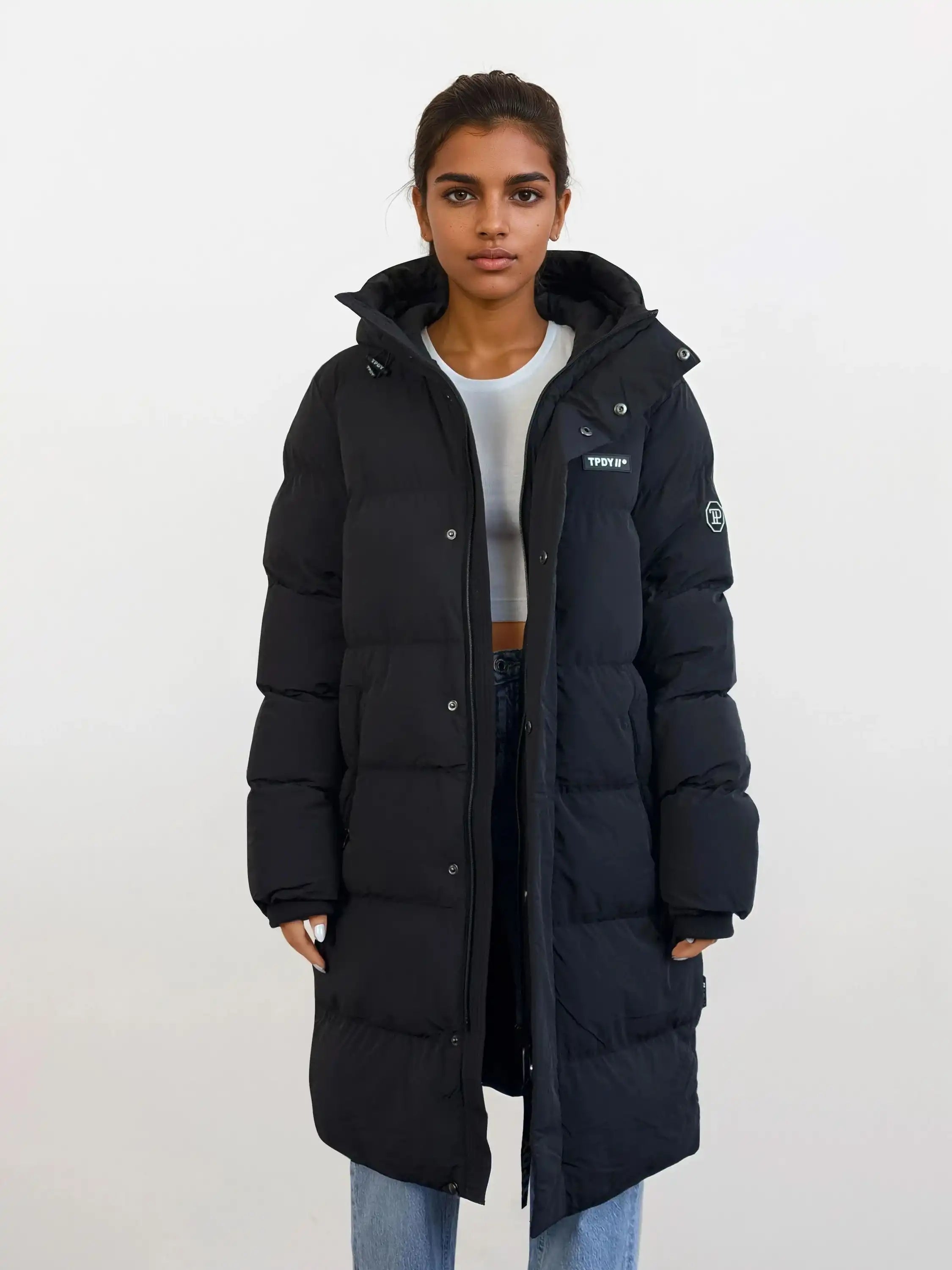 Eine Person trägt einen wasserabweisenden Damen Parka mit fester Kapuze im Regular Fit von trueprodigy über einem hellgrauen kurzen Top und blauen Jeans. Der Parka hat Patches an Brust und Ärmel.