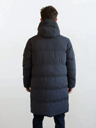 Eine Person steht mit dem Rücken zur Kamera und trägt den Herren Parka mit fester Kapuze im Regular Fit von trueprodigy; der wasserabweisende Mantel hebt sich vor einem schlichten, hellen Hintergrund ab.