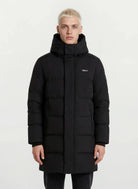 Ein Mann trägt den trueprodigy Herren Parka mit fester Kapuze im Regular Fit in Schwarz, mit kleinem Logo auf der linken Brust und seitlichen Reißverschlusstaschen, vor einem schlichten weißen Hintergrund. Der Mantel ist wasserabweisend.