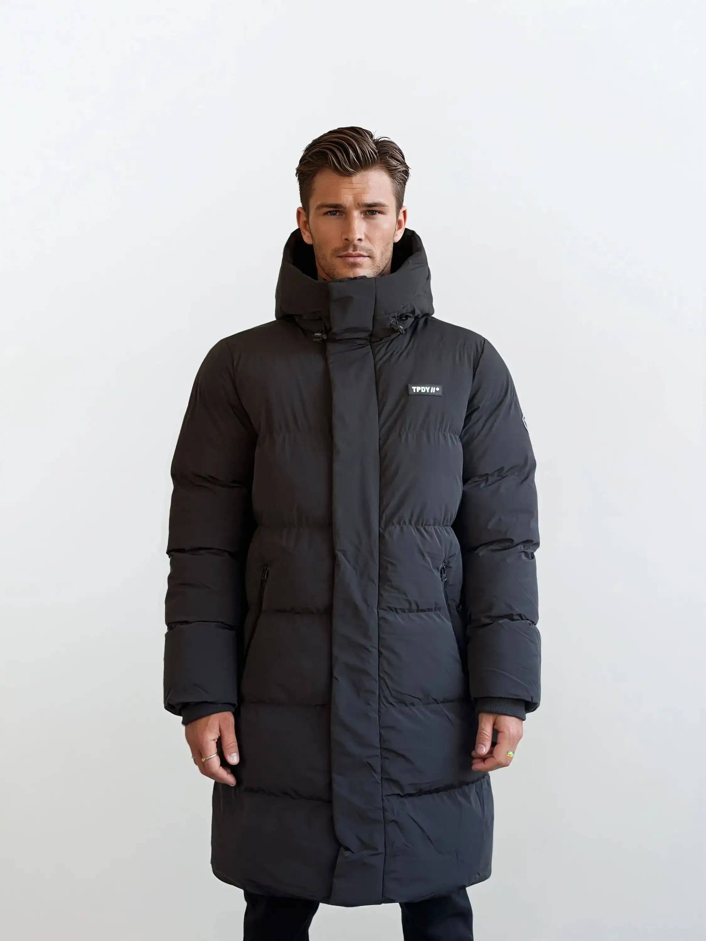 Vor weißem Hintergrund trägt ein Mann den Herren Parka mit fester Kapuze im Regular Fit von trueprodigy. Der wasserabweisende Parka hat sichtbare Nähte, ein kleines weißes Logo auf der linken Brust und die Hände des Mannes ruhen an seinen Seiten.