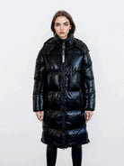 Eine Frau mit glattem braunem Haar und neutralem Gesichtsausdruck modelliert die trueprodigy Damen Winterjacke mit hochglänzender Oberfläche im Regular Fit, vorne mit Reißverschluss und abnehmbarer Kapuze, über einer schwarzen Hose vor einem schlichten weißen Hintergrund.