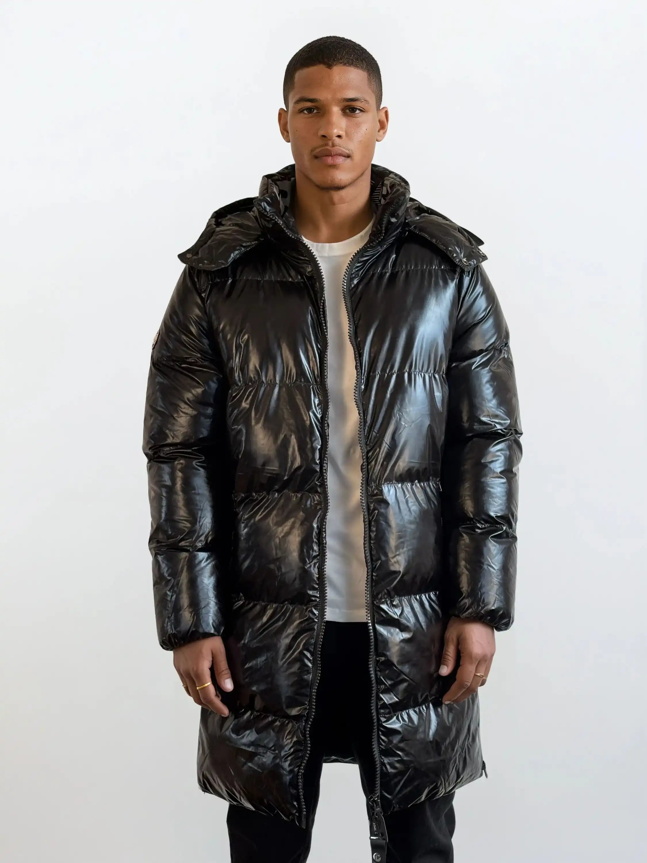 Eine Person steht mit dem Gesicht nach vorne und trägt eine trueprodigy Herren Winterjacke mit hochglänzender Oberfläche im Regular Fit über einem hellen Hemd und einer dunklen Hose vor einem schlichten weißen Hintergrund.