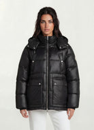 Eine Person steht mit dem Gesicht nach vorne und trägt die trueprodigy Damen Winterjacke mit hochglänzender Oberfläche im Regular Fit über einer weißen Hose vor einem schlichten hellen Hintergrund.