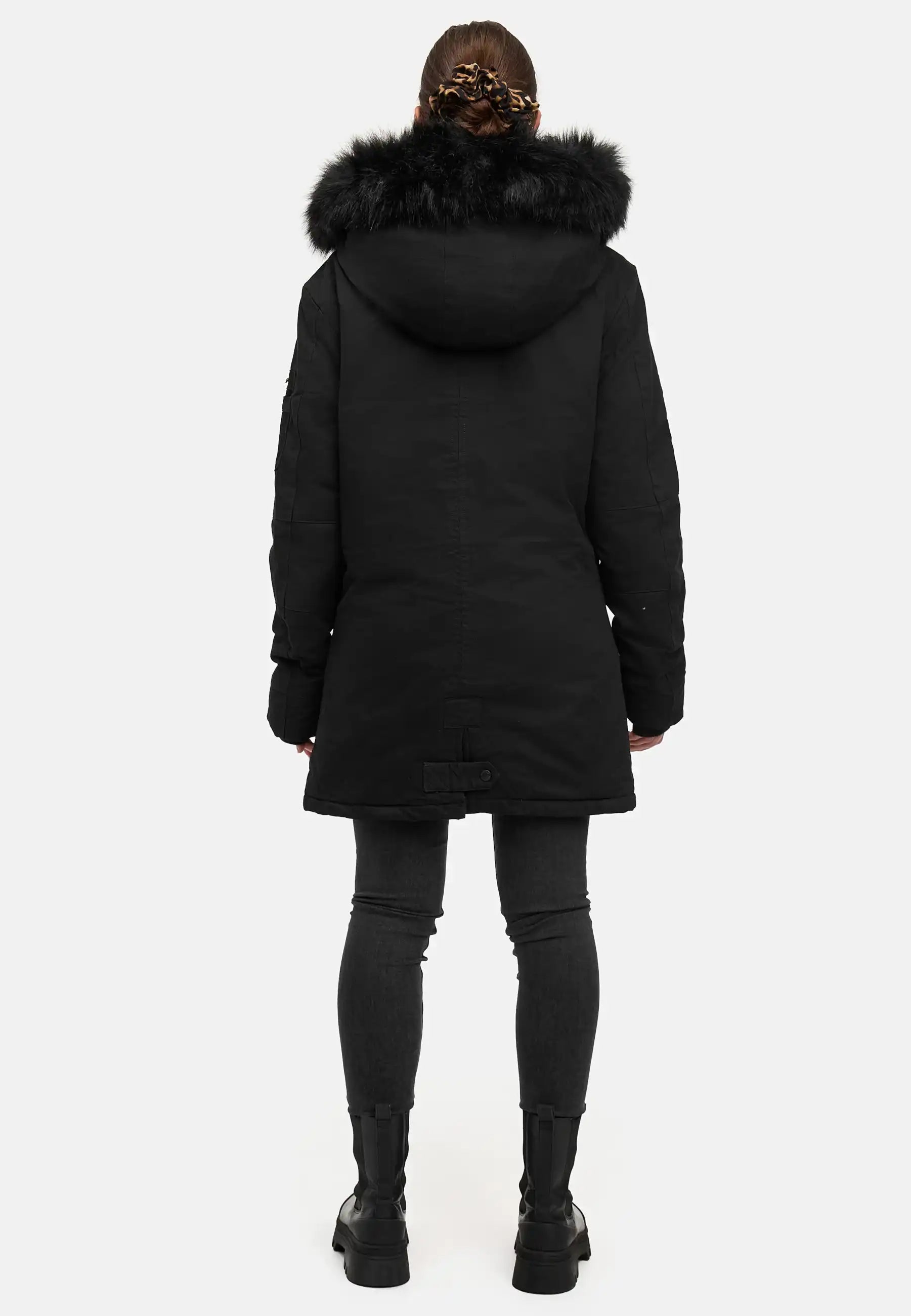 Eine Person steht mit dem Gesicht zur Wand und trägt den trueprodigy Julius F Parka mit Kapuze und Kunstfell, gepaart mit einer schwarzen Hose und Stiefeln. Die Haare sind hochgesteckt und ein schlichter weißer Hintergrund unterstreicht die lässige Passform des Parkas.