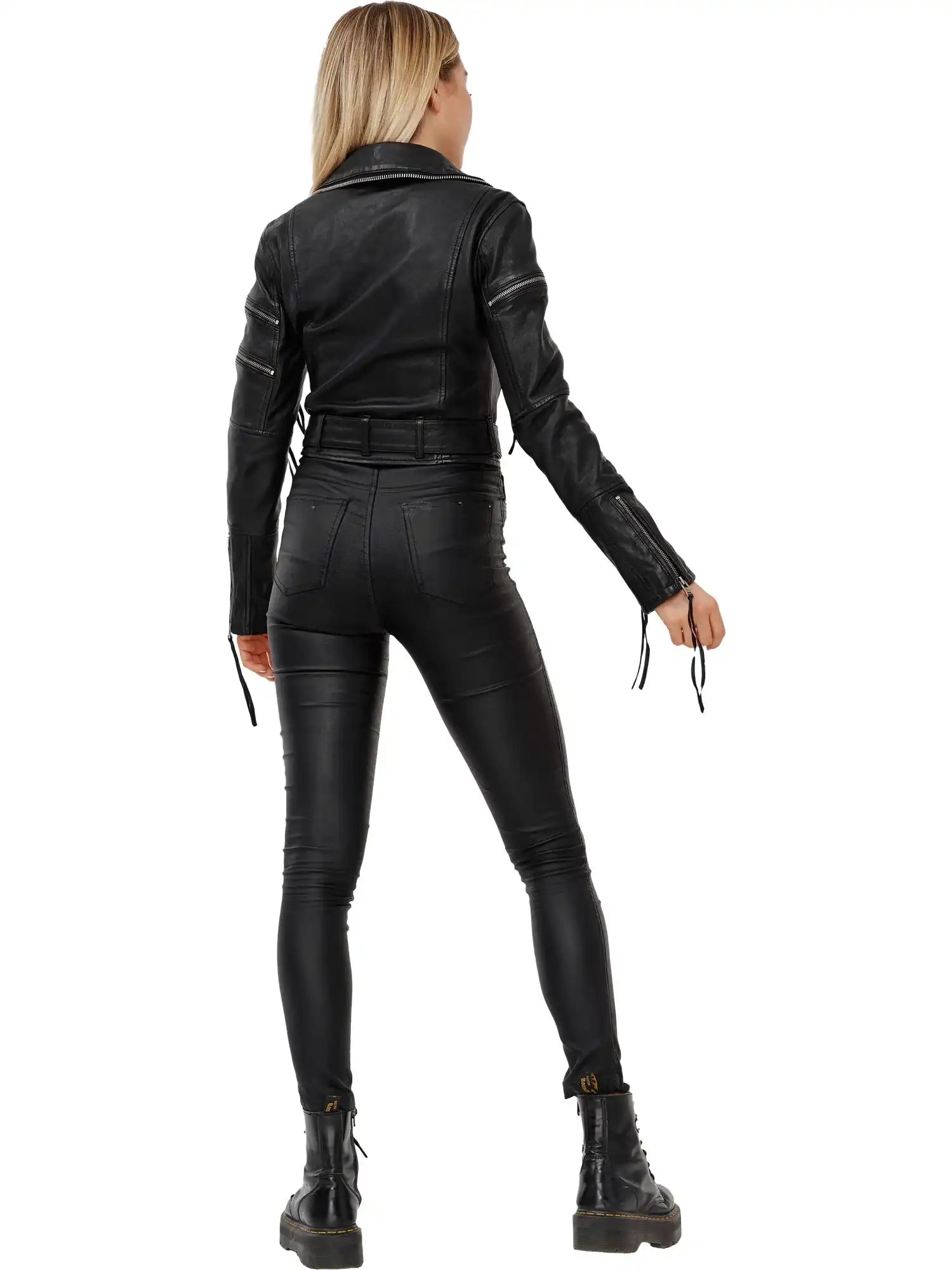 Eine Person mit langen blonden Haaren, von hinten gesehen, trägt die Izzy Bikerlederjacke mit Gürtel von trueprodigy, schwarze Skinny-Hosen und schwarze Schnürstiefel und steht vor einem schlichten weißen Hintergrund.