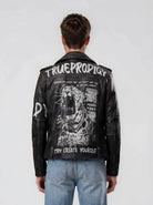 Eine Person in hellblauen Jeans und einer schwarzen Trueprodigy Biker Lederjacke Herren "Russell" mit Rücken-Print - mit Text und einer rasanten Leopardengrafik - zeigt einen gewagten Biker-Look, von hinten gesehen vor einem schlichten, hellen Hintergrund.