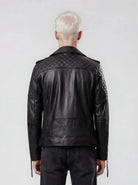 Eine Person mit kurzen, platinblonden Haaren ist von hinten zu sehen. Sie trägt die trueprodigy Biker Lederjacke Herren "Simba" mit Gürtel und schwarze Jeans und steht vor einem schlichten hellgrauen Hintergrund.