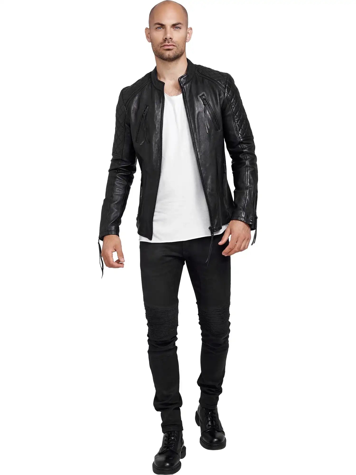 Ein Mann mit rasiertem Kopf, der eine Trueprodigy Simba Bikerlederjacke mit Gürtel, ein weißes T-Shirt, schwarze Jeans und schwarze Stiefel trägt, steht vor einem weißen Hintergrund.