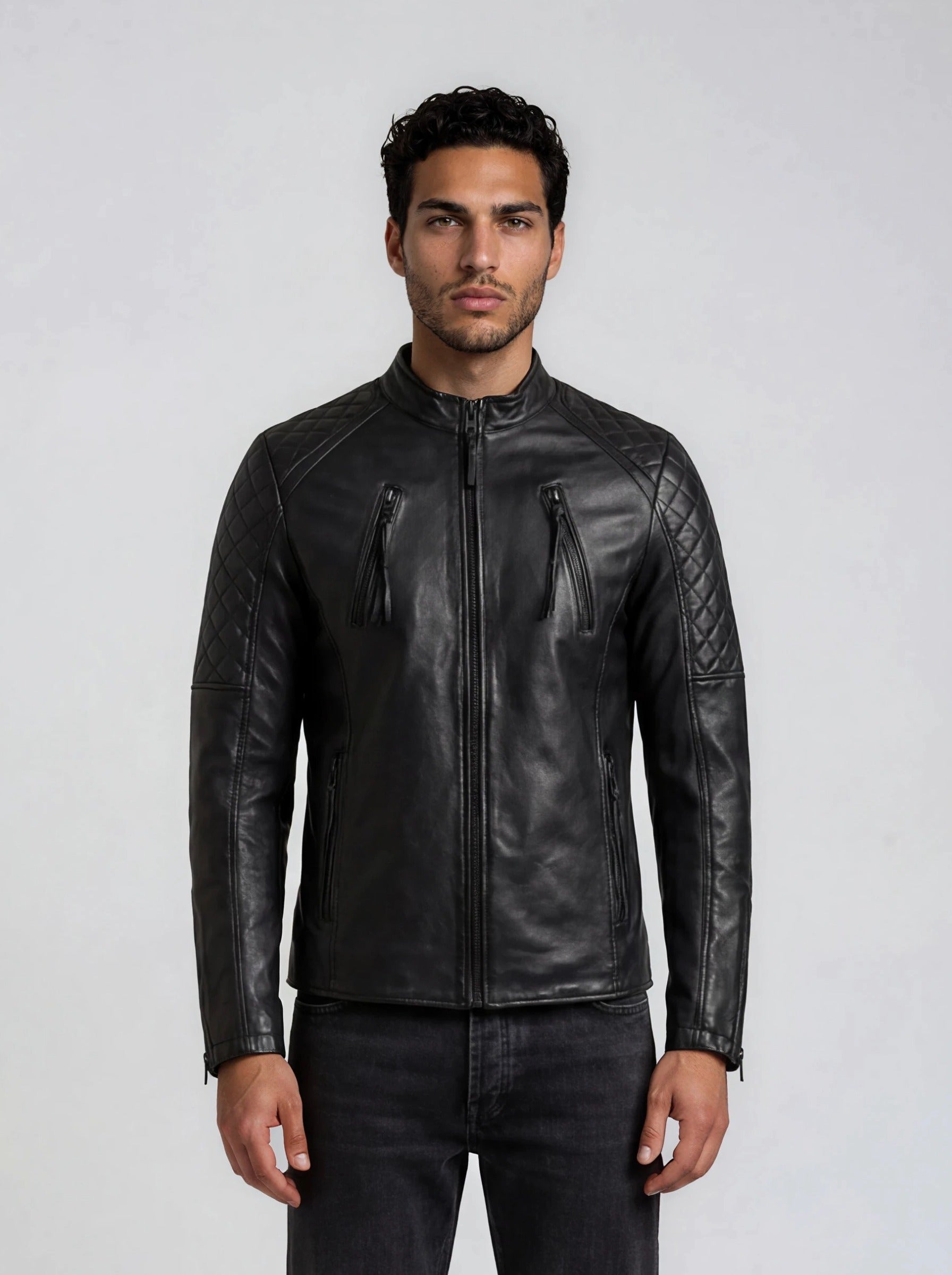 Ein Mann steht vor einem schlichten hellen Hintergrund und trägt die trueprodigy Racing Lederjacke Herren "Franky" in schwarz mit Rautensteppung an Schultern und Oberarmen, zwei vertikalen Reißverschluss-Brusttaschen, gepaart mit einer schwarzen Jeans.