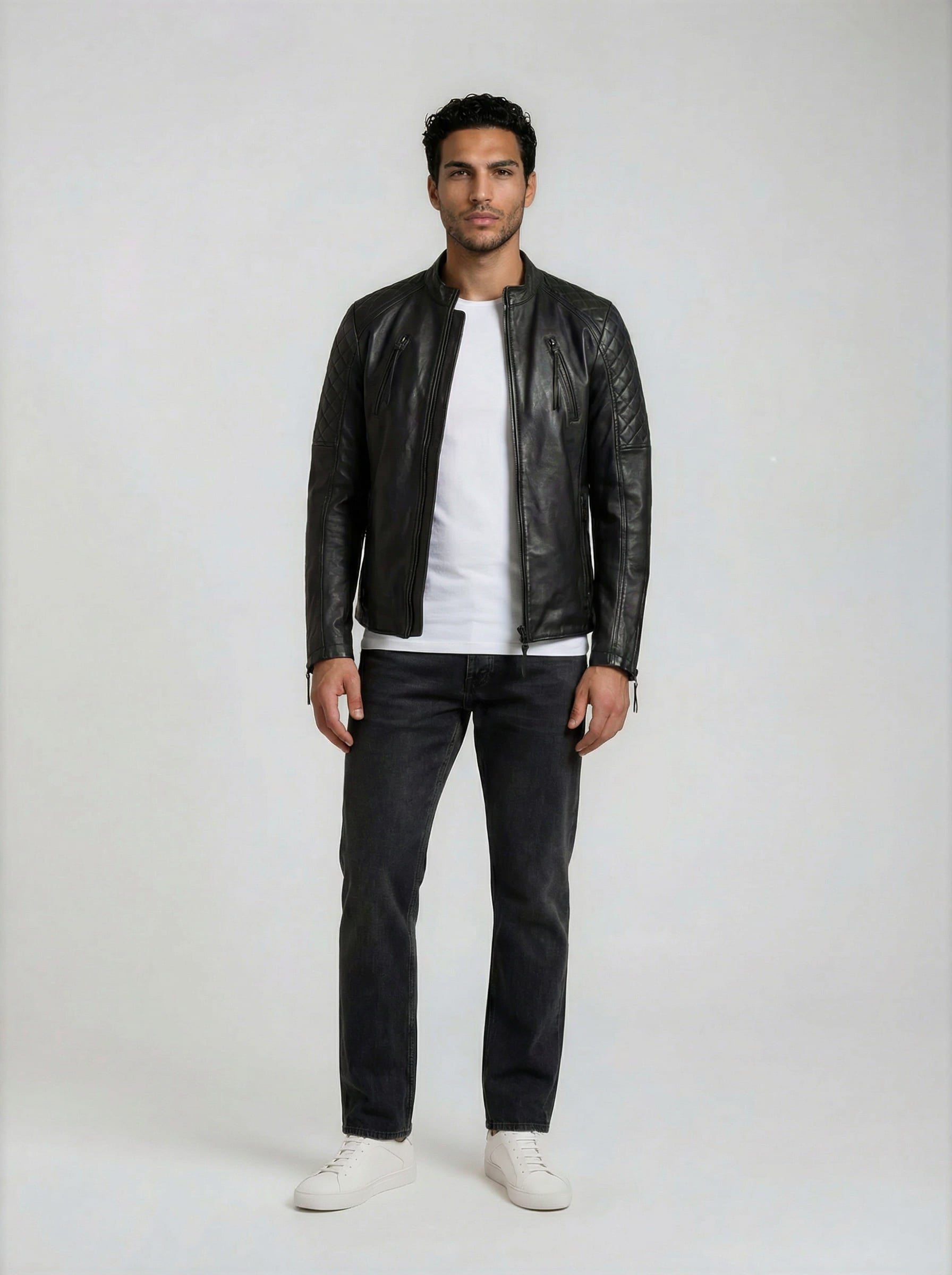 Ein Mann schaut nach vorne und trägt die trueprodigy Racing Lederjacke Herren "Franky" mit Rautensteppung, gestylt mit weißem T-Shirt, dunkler Jeans und weißen Turnschuhen vor einem schlichten hellen Hintergrund.