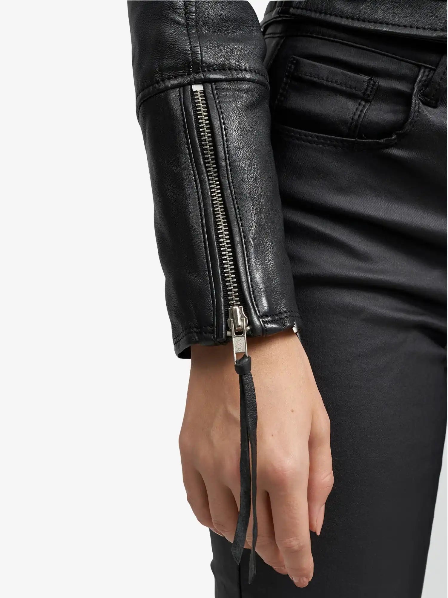 Eine Person trägt eine schwarze Hose und die trueprodigy Laila Lederjacke mit Druck, die mit ihrem schicken silbernen Ärmelreißverschluss für einen echten Trend-Look sorgt. Der lässige linke Arm unterstreicht dieses stylische Detail der Jacke.