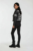 Eine Frau steht in Dreiviertel-Pose mit Blick nach links und trägt die trueprodigy Lederjacke mit Druck mit weißer Grafik auf dem Rücken, gepaart mit schwarzen Skinny Jeans und Schnürstiefeln vor einem schlichten weißen Hintergrund.