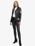 Eine Person trägt die Laila Lederjacke mit Druck von trueprodigy über einem weißen T-Shirt, dazu schwarze Skinny Pants und schwarze heeled Ankle Boots. Sie hat lange, glatte Haare und einen neutralen Gesichtsausdruck.
