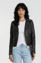 Eine Frau mit gewelltem dunklem Haar trägt die trueprodigy Lederjacke mit Gürtel über einem weißen T-Shirt und hellblauen Jeans und steht mit dem Gesicht nach vorne vor einem schlichten weißen Hintergrund.